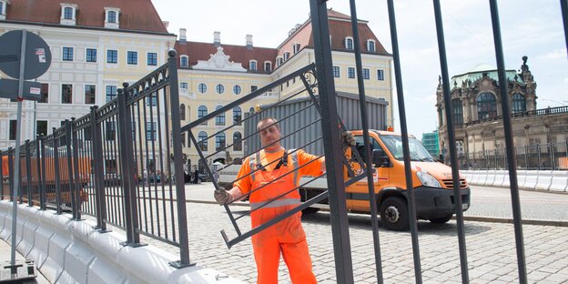 Mann in orangenem Overall montiert Zaun vor Gebäude in Dresden Mann in orangenem Overall montiert Zaun vor Gebäude in Dresden
