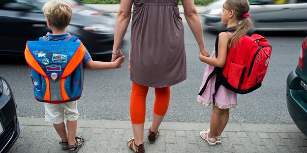 Mutter mit zwei Kinder an der Hand steht an der Straße Mutter mit zwei Kinder an der Hand steht an der Straße
