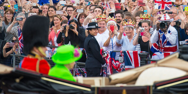 Queen Eilzabeth II. in einem froschgrünen Kostüm in einer Kutsche, dahinter jubelnde Menschen Queen Eilzabeth II. in einem froschgrünen Kostüm in einer Kutsche, dahinter jubelnde Menschen