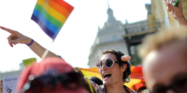 Mann mit Sonnenbrille, Penishaarreif und Discokugel-Ohrringen auf einer Gay-Pride in Sofia, Bulgarien. Im Hintergrund ist eine Regenbogenflagge. Mann mit Sonnenbrille, Penishaarreif und Discokugel-Ohrringen auf einer Gay-Pride in Sofia, Bulgarien. Im Hintergrund ist eine Regenbogenflagge.