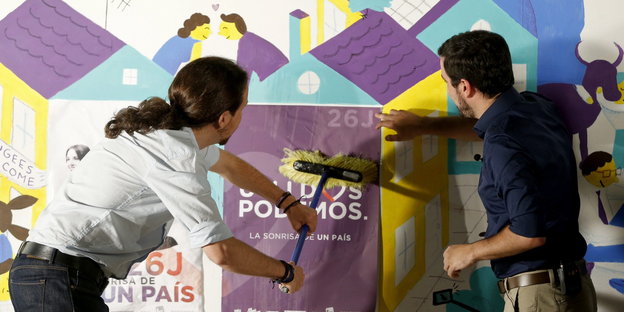 Zwei Männer kleben gemeinsam Plakate an die Wand, links zu sehen: der Podemos-Chef Pablo Iglesias