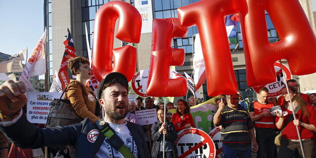 Menschen protestieren mit Schildern und roten Luftkissen, die die Buchstaben „CETA“ bilden Menschen protestieren mit Schildern und roten Luftkissen, die die Buchstaben „CETA“ bilden