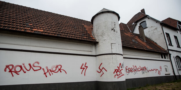 An einer weißen Hauswand sind mit roter Farbe Hakenkreuze geschmiert und Beschimpfungen geschmiert