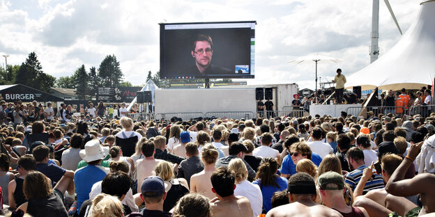Eine Menschenmenge unter freiem Himmel schaut auf eine Videoleinwand, auf der Snowden zu sehen ist Eine Menschenmenge unter freiem Himmel schaut auf eine Videoleinwand, auf der Snowden zu sehen ist