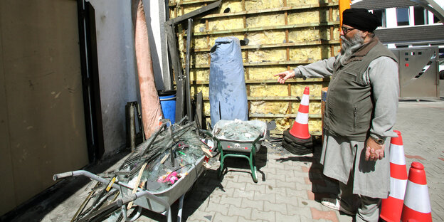 Ein Mann mit Haartuch steht Schubkarren und Warnhütchen Ein Mann mit Haartuch steht Schubkarren und Warnhütchen