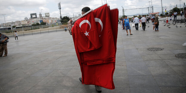 Ein Verkäufer trägt mehrere türkische Flaggen über einen Platz Ein Verkäufer trägt mehrere türkische Flaggen über einen Platz