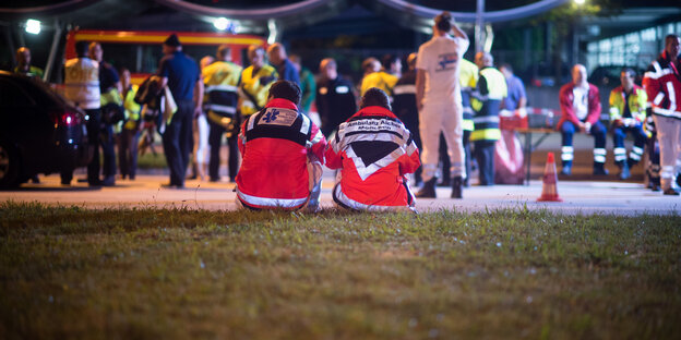 Zwei Menschen mit Rettungswesten sitzen auf einer Wiese Zwei Menschen mit Rettungswesten sitzen auf einer Wiese