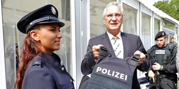 Joachim Herrmann hält eine schutzsichere Weste, daneben steht eine Polizistin Joachim Herrmann hält eine schutzsichere Weste, daneben steht eine Polizistin