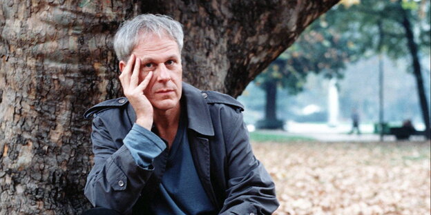 Der Schriftsteller Dennis Cooper sitzt vor einem Baum und stützt seinen Kopf in seine Hand Der Schriftsteller Dennis Cooper sitzt vor einem Baum und stützt seinen Kopf in seine Hand