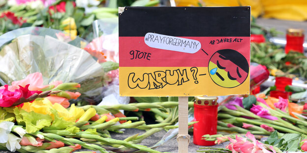 Eine Deutschlandfahne mit der Aufschrift "Warum" zwischen Blumen und Kerzen Eine Deutschlandfahne mit der Aufschrift "Warum" zwischen Blumen und Kerzen