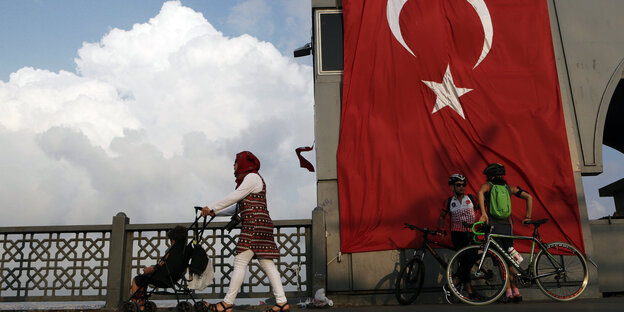 Eine Frau schiebt einen Kinderwagen über die Galata-Brücke in Istanbul, die mit einer riesigen Türkei-Fahne geschmückt ist. Eine Frau schiebt einen Kinderwagen über die Galata-Brücke in Istanbul, die mit einer riesigen Türkei-Fahne geschmückt ist.