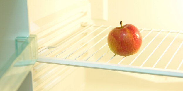 Ein Apfel liegt in einem ansonsten leeren Kühlschrank Ein Apfel liegt in einem ansonsten leeren Kühlschrank