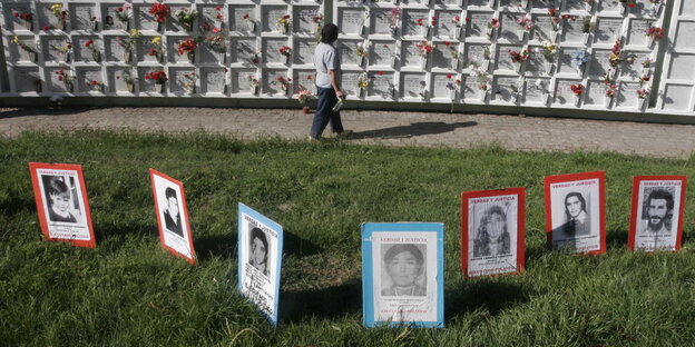 eine Wand mit Urnengräbern, davor Pappschilder mit Porträtaunahmen eine Wand mit Urnengräbern, davor Pappschilder mit Porträtaunahmen