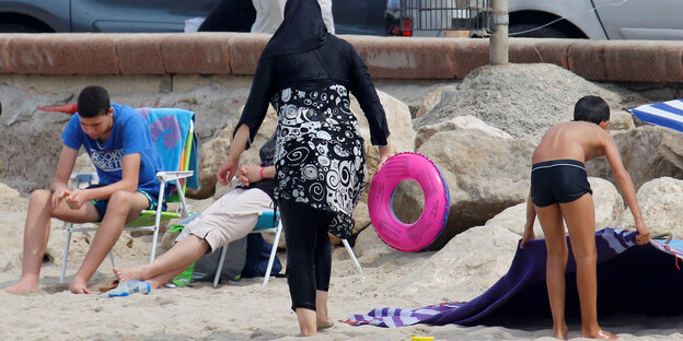 Eine Frau trägt ein langes Hemd und ein Kopftuch an einem Strand Eine Frau trägt ein langes Hemd und ein Kopftuch an einem Strand