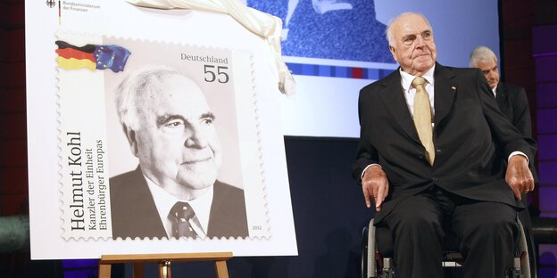 Helmut Kohl sitzt im Rollstuhl neben einer sehr großen Helmut-Kohl-Briefmarke Helmut Kohl sitzt im Rollstuhl neben einer sehr großen Helmut-Kohl-Briefmarke
