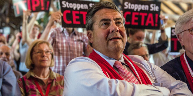 Im Vordergrund ein Mann mit roter Weste, im Hintergrund Protestschilder gegen Ceta Im Vordergrund ein Mann mit roter Weste, im Hintergrund Protestschilder gegen Ceta