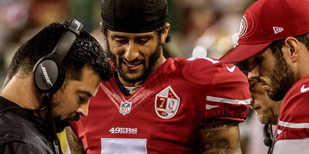Ein Mann in Football-Schutzkleidung mit ausgepolsterten Schultern und einer schwarzen Kopfbedeckung Ein Mann in Football-Schutzkleidung mit ausgepolsterten Schultern und einer schwarzen Kopfbedeckung