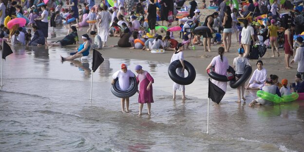 Menschen in Badebekleidung stehen am Strand im Wasser Menschen in Badebekleidung stehen am Strand im Wasser