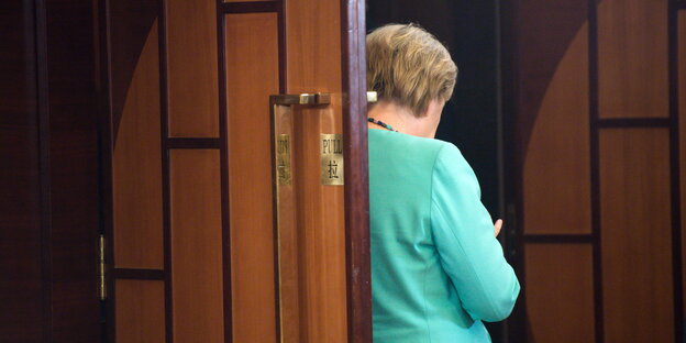 Angela Merkel steht mit dem Rücken zum Fotografen an der Tür eines Besprechungsraums in Hangzhou und schaut auf ihr Smartphone Angela Merkel steht mit dem Rücken zum Fotografen an der Tür eines Besprechungsraums in Hangzhou und schaut auf ihr Smartphone