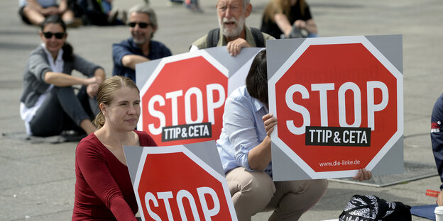 Protestierende sitzen mit Stop-Ceta/TTIP-Schildern auf dem Boden Protestierende sitzen mit Stop-Ceta/TTIP-Schildern auf dem Boden