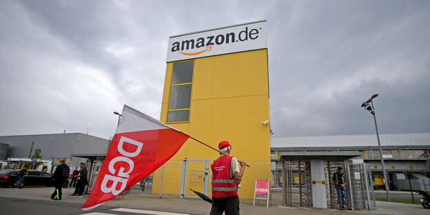 Mann mit DGB-Fahne vor einen Amazon-Firmentor Mann mit DGB-Fahne vor einen Amazon-Firmentor