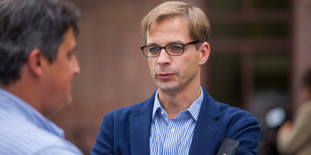 Ein Mann in blauem Anzug mit Brille und hellen Haaren