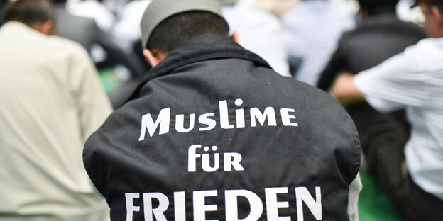 Ein Mann trägt den Kopf gesenkt und den Schriftzug Muslime für Frieden auf dem Rücken Ein Mann trägt den Kopf gesenkt und den Schriftzug Muslime für Frieden auf dem Rücken