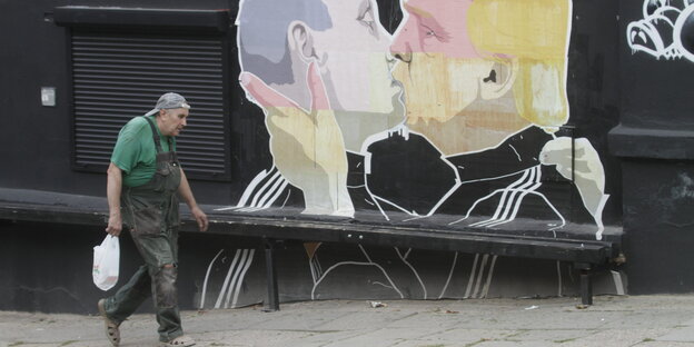 Ein Mann läuft vor einem Grafitti entlang, das Wladimir Putin und Donald Trump dabei zeigt wie sie sich innig küssen Ein Mann läuft vor einem Grafitti entlang, das Wladimir Putin und Donald Trump dabei zeigt wie sie sich innig küssen