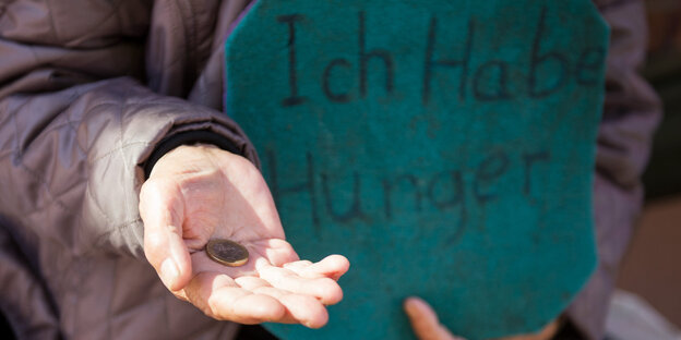 Eine ausgestreckte Hand, auf der eine Münze liegt, daneben ein Schild „Ich habe Hunger“ Eine ausgestreckte Hand, auf der eine Münze liegt, daneben ein Schild „Ich habe Hunger“