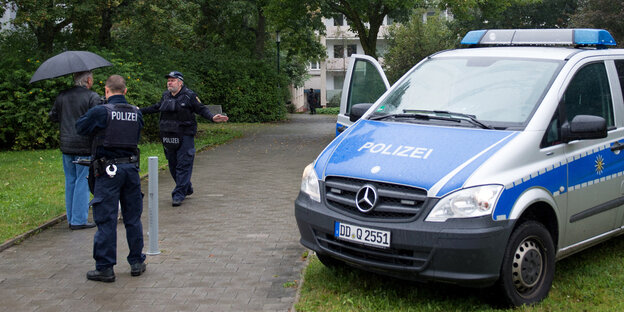 Ein Mann mit Schirm spricht mit zwei Polizisten Ein Mann mit Schirm spricht mit zwei Polizisten