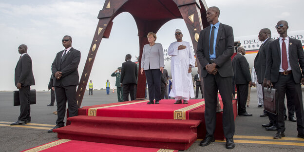 Angela Merkel steht neben Ibrahim Boubakar auf einem roten Teppich unter einem Baldachin Angela Merkel steht neben Ibrahim Boubakar auf einem roten Teppich unter einem Baldachin