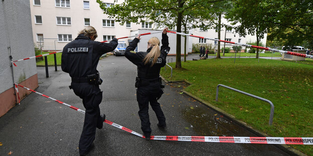Zwei Polizisten gehen unter einem Absperrband hindurch zu einem Wohnhaus Zwei Polizisten gehen unter einem Absperrband hindurch zu einem Wohnhaus