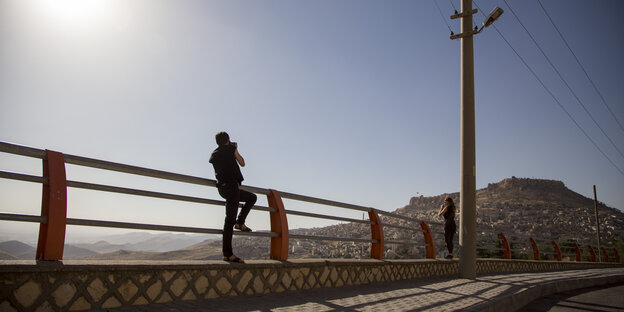 Zwei Menschen auf einer Brücke vor Landschaft