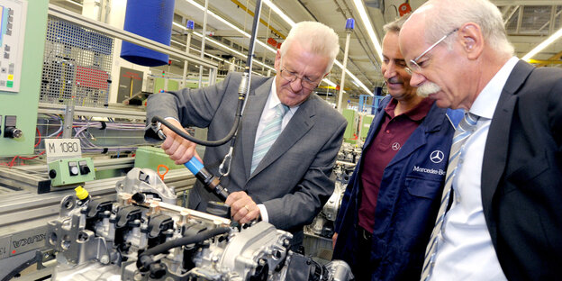 Winfried Kreschtmann schraubt an einem Motor, Dieter Zetsche schaut zu Winfried Kreschtmann schraubt an einem Motor, Dieter Zetsche schaut zu