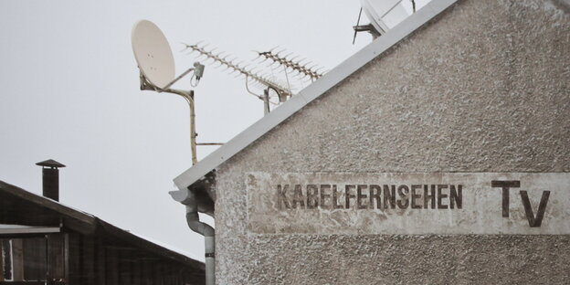 Auf einem Haus mit Satellitenschüsseln steht "Kabelfernsehen TV" Auf einem Haus mit Satellitenschüsseln steht "Kabelfernsehen TV"