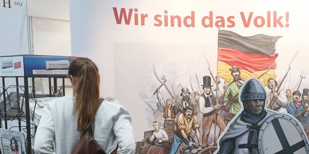 Eine Frau am Stand der Jungen Freiheit, im Hintergrund ein Pappaufsteller, auf dem „Wir sind das Volk“ steht Eine Frau am Stand der Jungen Freiheit, im Hintergrund ein Pappaufsteller, auf dem „Wir sind das Volk“ steht