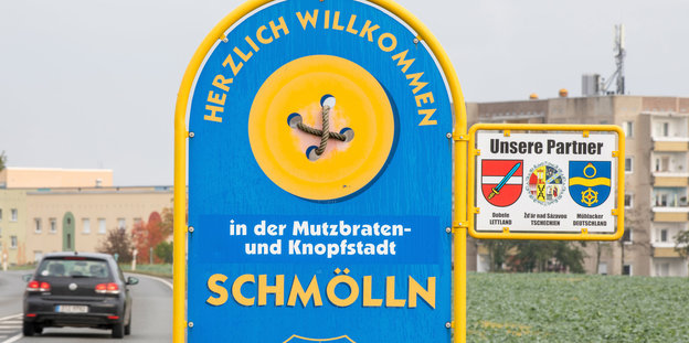 Schild an Straße, Aufschrift "Herzlich willkommen in der Mutzbraten- und Knopfstadt Schmölln"