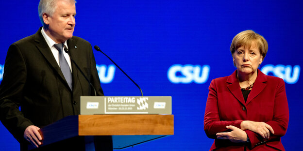 Sehofer steht an einem Rednerpult. Merkel daneben. Im Hintergrund eine blaue Wand mit dem Schriftzug CSU Sehofer steht an einem Rednerpult. Merkel daneben. Im Hintergrund eine blaue Wand mit dem Schriftzug CSU