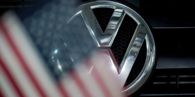 Ein Logo an einem VW-Auto zeichnet sich hinter einer USA-Fahne ab Ein Logo an einem VW-Auto zeichnet sich hinter einer USA-Fahne ab