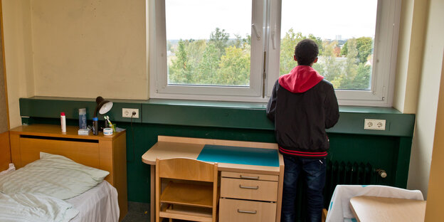 Junge steht am Fenster eines Wohnheimzimmers Junge steht am Fenster eines Wohnheimzimmers
