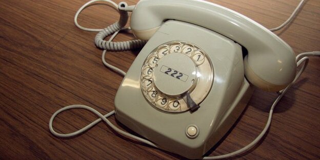 Ein altes graues Wählscheibentelefon auf einem braunen Furniertisch. Ein altes graues Wählscheibentelefon auf einem braunen Furniertisch.