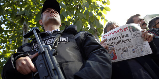 Hinter einem Polizisten mit Gewehr hält ein Mann die Cumhuriyet in die Höhe Hinter einem Polizisten mit Gewehr hält ein Mann die Cumhuriyet in die Höhe
