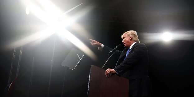 Donald Trump spricht, stützt sich mit dem linken Arm auf ein Pult und zeigt mit dem rechten nach vorne Donald Trump spricht, stützt sich mit dem linken Arm auf ein Pult und zeigt mit dem rechten nach vorne