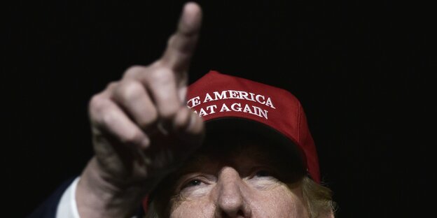 Donald Trump trägt eine rote Baseball-Kappe und streckt den Zeigefinger in die Luft Donald Trump trägt eine rote Baseball-Kappe und streckt den Zeigefinger in die Luft