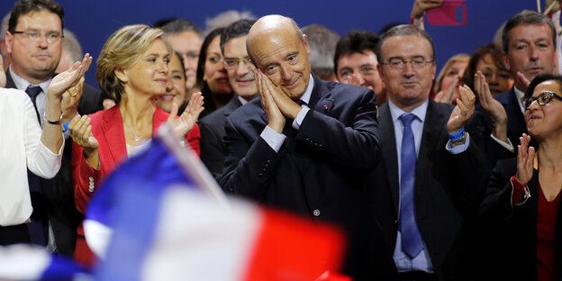 Alain Juppe in der Mitte einer Gruppe von Menschen, er legt seine Hände an die Schläfe Alain Juppe in der Mitte einer Gruppe von Menschen, er legt seine Hände an die Schläfe