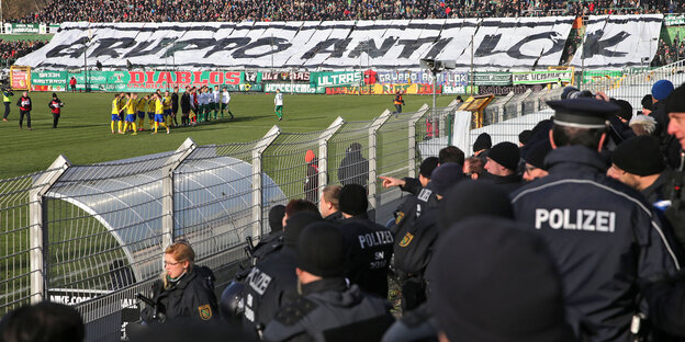 Viele Polizisten stehen auf einer Stadiontribüne, im Hintergrund sieht man das Spielfeld Viele Polizisten stehen auf einer Stadiontribüne, im Hintergrund sieht man das Spielfeld