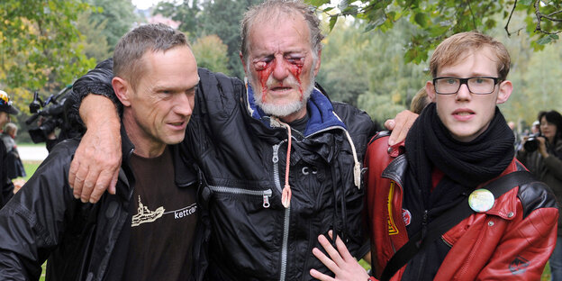 Zwei junge Männer tragen eine älteren, der aus den Augen blutet Zwei junge Männer tragen eine älteren, der aus den Augen blutet