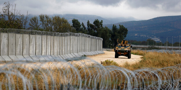 Ein gepanzertes türkisches Militärfahrzeug fährt an einer Mauer an der türkisch-syrischen Grenze entlang, im Vordergrund ist Stacheldraht zu sehen Ein gepanzertes türkisches Militärfahrzeug fährt an einer Mauer an der türkisch-syrischen Grenze entlang, im Vordergrund ist Stacheldraht zu sehen