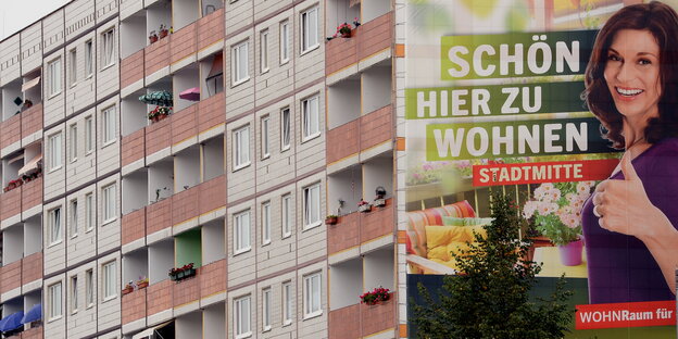 ein Plattenbau auf dessen Seite ein großes Plakat auf dem steht „Schön hier zu wohnen“ ein Plattenbau auf dessen Seite ein großes Plakat auf dem steht „Schön hier zu wohnen“