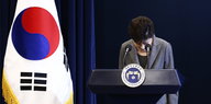 Park Geun-Hye verbeugt sich hinter einem Stehpult, daneben die Fahne Südkoreas
